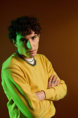 Şık bir adam, parlak sarı bir süveter ve eşsiz aksesuarlar giyerken kendine güvenerek poz verir..