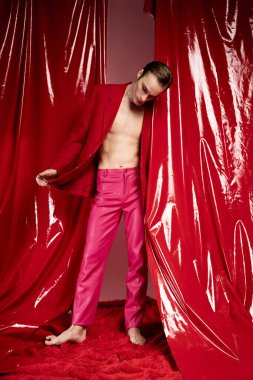 Bir adam zarif bir şekilde canlı kırmızı perdelerin arasında duruyor, cesur bir kıyafetle aşkı kutluyor..
