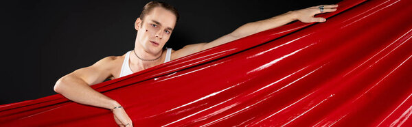 A young man embraces Valentines Day with a radiant red backdrop, showcasing love and identity.