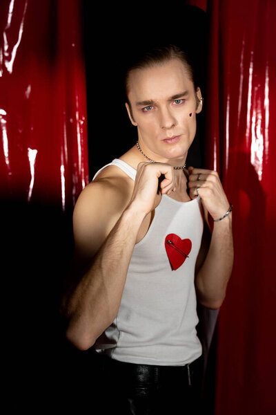 A confident man in a white tank top with a red heart joyfully celebrates Valentine Day.