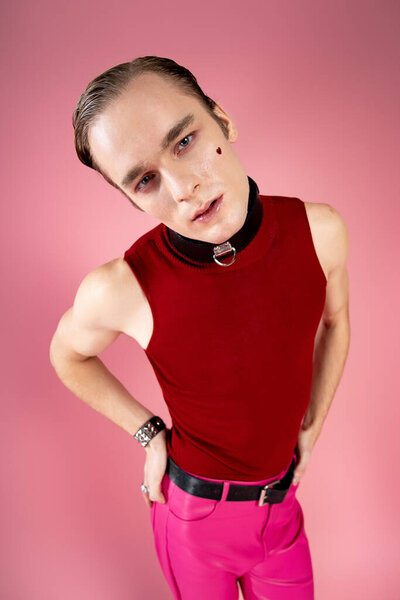 A stylish man poses confidently in a striking outfit against a bright pink backdrop, embodying love.