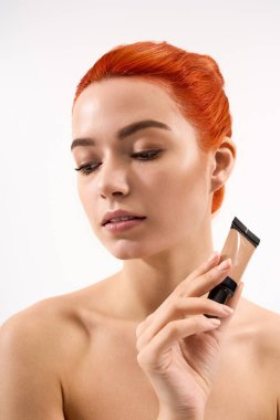 Canlı kızıl saçlı genç bir kadın doğal güzellik ve tarz sergileyerek makyajı keşfediyor..