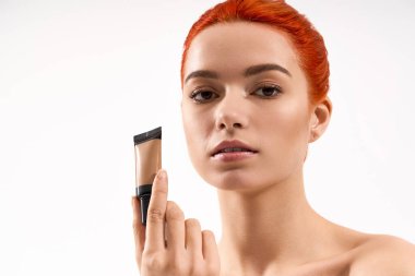 Kendine güvenen makyajlı genç bir kadın temel tutarken güzellik rutinini ön plana çıkarıyor..