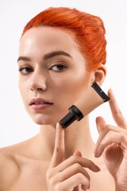 Çekici kızıl saçlı güzel bir kadın zarif poz verirken makyaj uygulaması sergiliyor..