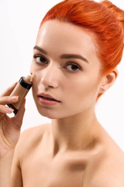 Hayat dolu saçları olan güzel genç bir kadın makyajını düşünceli bir şekilde parlak bir atmosferde yapar.