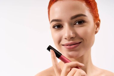 Çekici kızıl saçlı güzel bir kadın dudak rengini tutarken makyaj yeteneğini ön plana çıkarıyor..