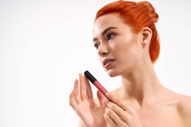 Kızıl saçlı çarpıcı bir kadın kendinden emin bir kozmetik ürünü tutuyor..