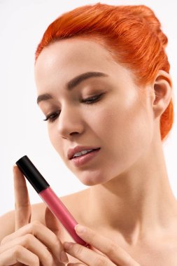 Parlak turuncu saçlı güzel bir kadın pembe rujunu test ediyor, kendinden emin..