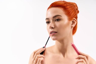 Güzel bir kadın, kendine güvenerek parlak dudak rengi uygulayarak makyaj yeteneklerini sergiler..