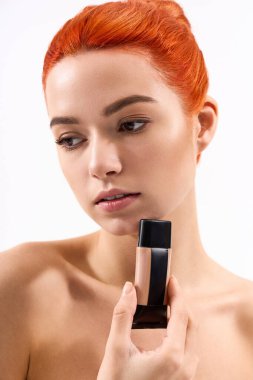 Hareketli saçlı şık bir kadın makyaj malzemesi tutuyor, narin ışıkta güzelliğini vurguluyor..