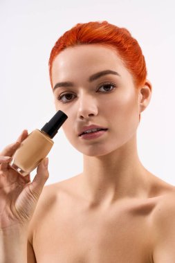 Genç bir kadın kusursuz cildini ve canlı stilini vurgulayan bir makyaj ürünü sunar..