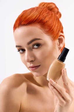 Turuncu saçlı güzel bir kadın makyaj şişesi tutuyor, zarafet ve tarz saçıyor..