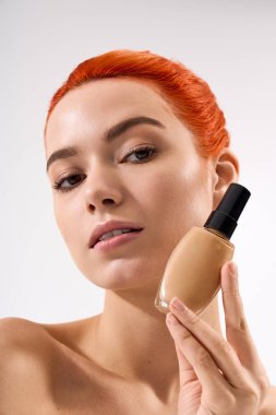 Parlak kızıl saçlı güzel bir kadın kusursuz cildini ön plana çıkarıyor. Temeli zarifçe tutuyor..