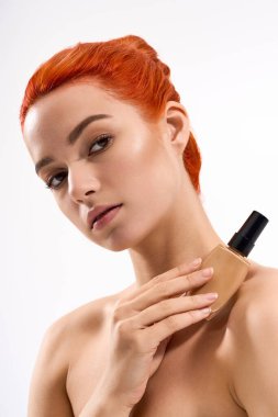 Genç, güzel bir kadın, makyaj ürününü, temiz bir arkaplanda ustalıkla sunar..