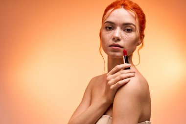 Çekici kadın zarif pozlar veriyor, güzelliğini göstererek cesur ruj ve çilli cildiyle..