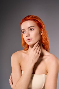 Çarpıcı turuncu saçlı genç kadın zarif poz veriyor, benzersiz makyajını ve tarzını vurguluyor..