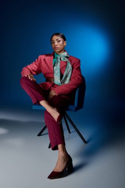 Genç bir kadın şık bir kıyafetle oturarak stüdyo ortamında modern modayı sergiliyor..