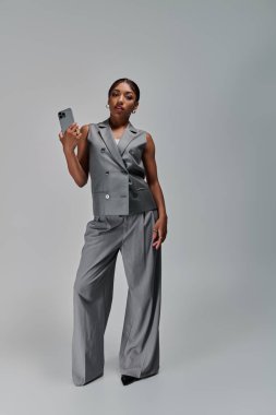 Genç bir Afrikalı Amerikalı kadın, elinde telefonuyla rahat bir şekilde poz veriyor..