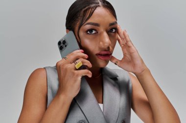 Kendine güvenen genç bir kadın, şık tarzını bir stüdyoda sergilerken elinde bir akıllı telefon tutuyor..