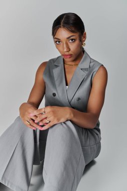 Moda kıyafetli genç bir kadın stüdyo ortamında otururken kendine güveniyor..