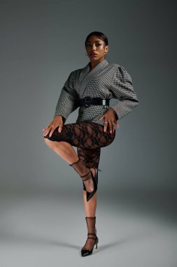 Genç bir kadın stüdyoda modellik yapıyor, kendine has tarzını ön plana çıkaran şık bir kıyafet giyiyor..