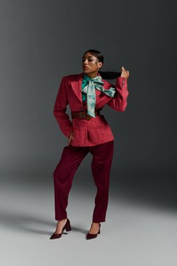 Kendine güvenen genç bir kadın modern bir stüdyo ortamında şık kıyafetlerini sergiliyor..