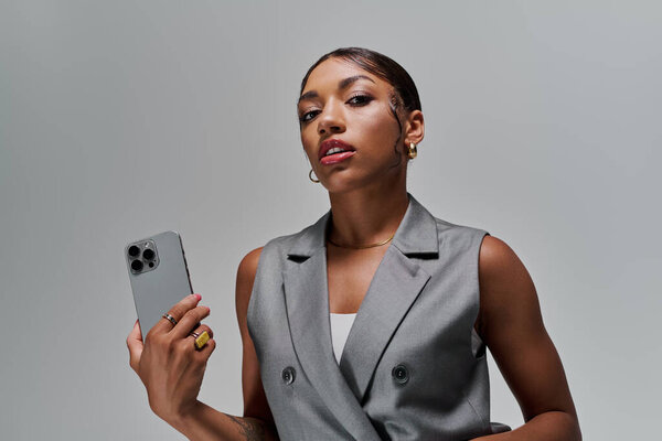 Стильная молодая женщина уверенно позирует со смартфоном, излучая элегантность в студии.