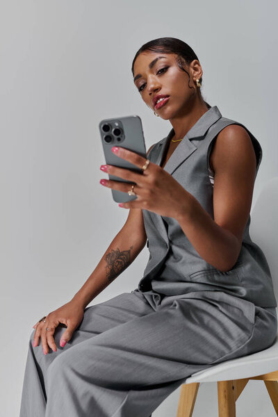 Молодая афроамериканка демонстрирует свою модную одежду, сидя в современной студии.