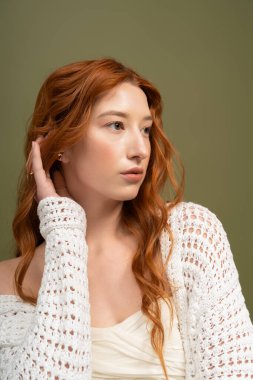 Genç kızıl saçlı bir kadın zarif bir şekilde stüdyo ortamında poz veriyor, modaya uygun bahar kıyafetleri giyiyor..