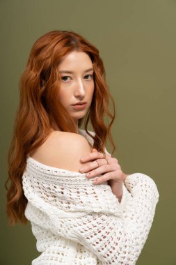 Göz kamaştırıcı kızıl saçlı genç bir kadın sakin bir stüdyoda şık bir bahar elbisesi giyiyor..