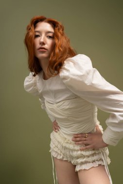 Kızıl saçlı genç kadın canlı bir stüdyo ortamında şık bahar kıyafetleri sergiliyor..