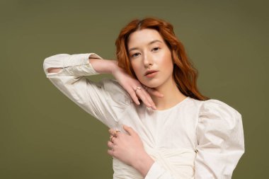 Kızıl saçlı genç bir kadın canlı bir stüdyo ortamında şık kıyafetler sergiliyor..