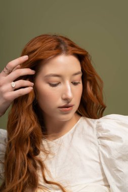 Çarpıcı kızıl saçlı genç bir kadın zarif poz veriyor, şık bahar kıyafetleri giyiyor..