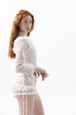 Şık giyinmiş genç bir kızıl zarif bir şekilde stüdyo ortamında poz veriyor..