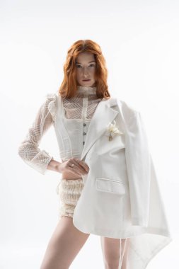 Canlı kızıl saçlı genç kadın sanatsal stüdyo ortamında şık bahar kıyafetleri sergiliyor..