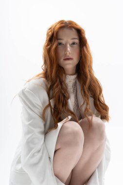 Kızıl saçlı genç bir kadın zarif bir şekilde poz veriyor. Parlak bir stüdyo içinde..