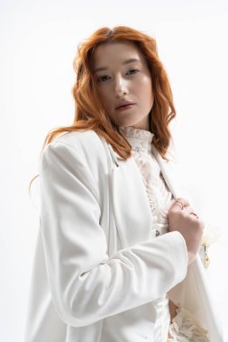 Şık giyinmiş genç bir kızıl, bahar havasını kucaklayan parlak bir stüdyoda güven içinde poz veriyor..