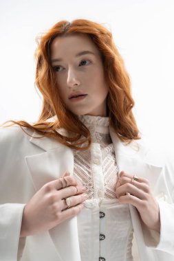 Güzel kızıl saçlı genç bir kadın şık bir bahar elbisesi içinde poz veriyor, kendine güveni tam.