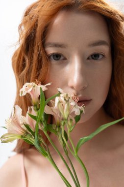 Kızıl saçlı genç bir kadın stüdyoda zarif çiçekler taşıyan şık bir kıyafet sergiliyor..