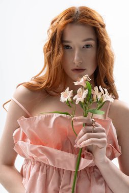Canlı kızıl saçlı genç bir kadın zarif bir bahar elbisesi içinde elinde çiçeklerle poz veriyor..