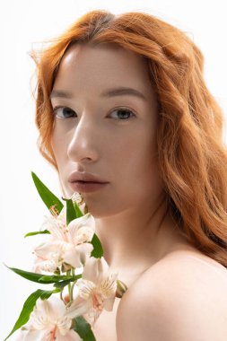 Genç kızıl saçlı bir kadın zarif çiçeklerle poz veriyor. Parlak bir stüdyoda bahar modasını sergiliyor..