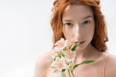 Çarpıcı kızıl saçlı genç bir kadın çiçeklerle zarifçe poz verir, bahar ruhunu yakalar..