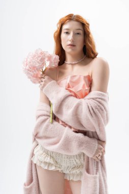 Genç kızıl saçlı bir kadın çiçeklerle zarifçe poz veriyor, bahar cazibesini somutlaştırıyor..