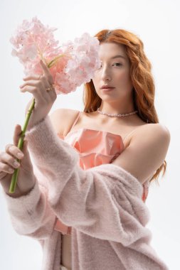 Kızıl saçlı genç kadın bahar çiçekleriyle bir stüdyoda zarif pozlar veriyor, tarzını sergiliyor..