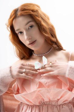 Kızıl saçlı genç bir kadın kelebekle poz verirken şık bir kıyafet sergiliyor.