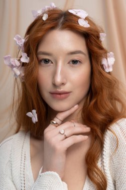 Moda kıyafetli parlak kızıl saçlı hoş bir stüdyoda zarif bir şekilde çiçeklerle poz veriyor..