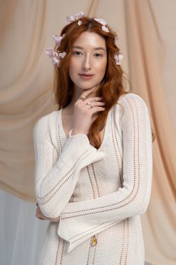 Uçan kızıl saçlı genç kadın çiçeklerle çevrili şık bir bahar görüntüsü sergiliyor..