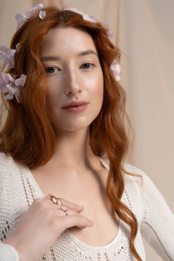 Genç bir kızıl saçlı bahar modasını sergiliyor. Stüdyoda çiçekler açıyor, büyüleyici bir cazibe yayıyor..