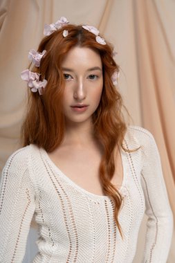 Genç bir kızıl güzel poz veriyor şık bir kıyafet içinde, bir stüdyoda çiçeklerle çevrili..