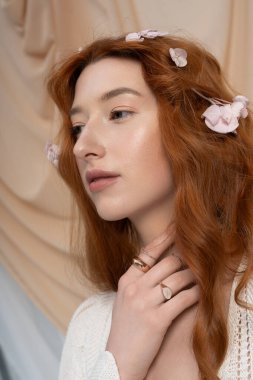 Canlı kızıl saçlı genç bir kadın zarif bir şekilde çiçeklerle poz veriyor, bahar özünü somutlaştırıyor..